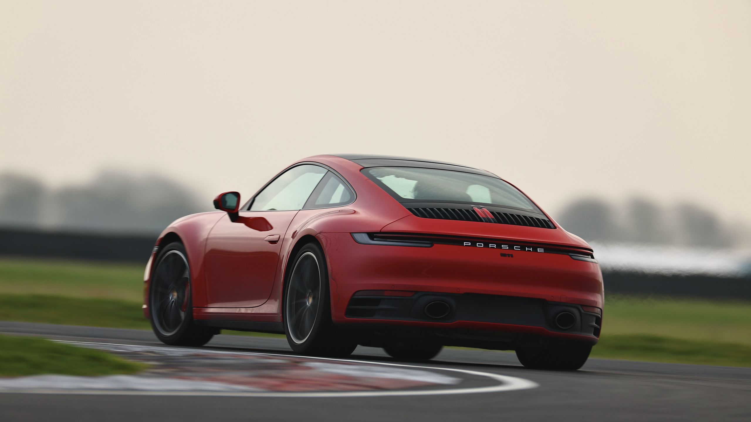 Red Porsche 911 (992) on track, seen from the rear showing its exhaust tailpipes